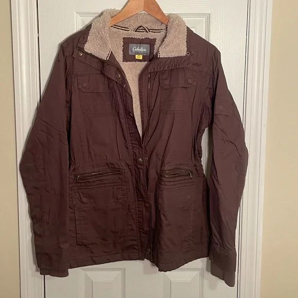 Een donkerbruine winterjas van Cabela's met teddy voering hangend aan een houten hanger.